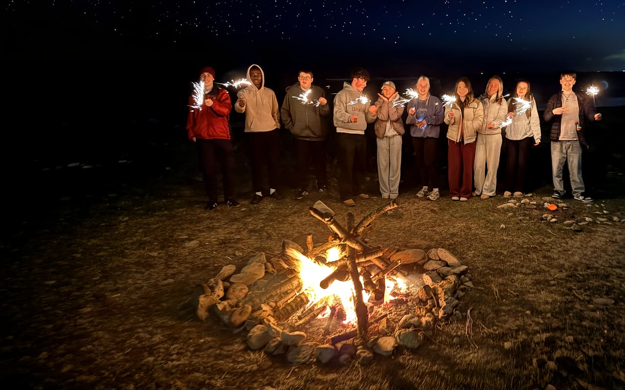 ROOT 66 students gathered around a campfire holding sparklers under a starry night sky on the Sunderland coast